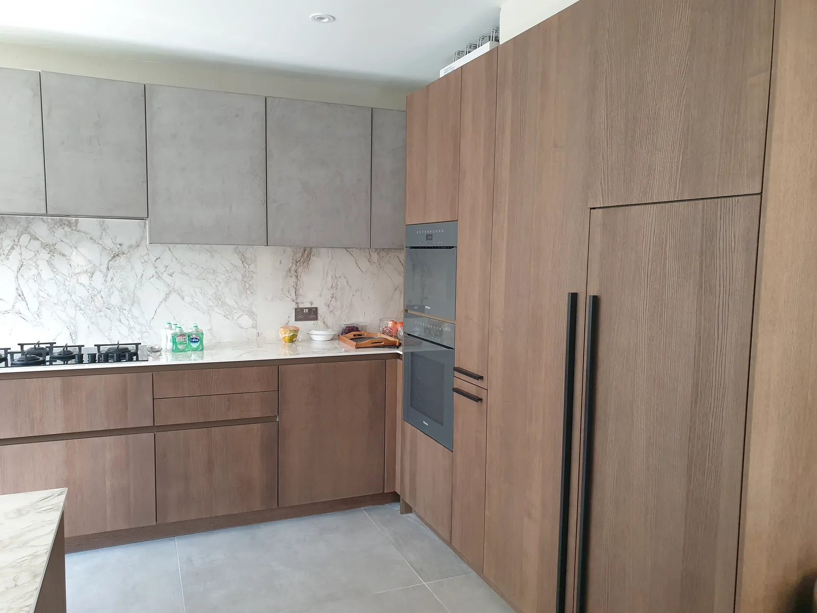 Wood-finish fitted kitchen cabinetry with integrated ovens and marble-effect splashback