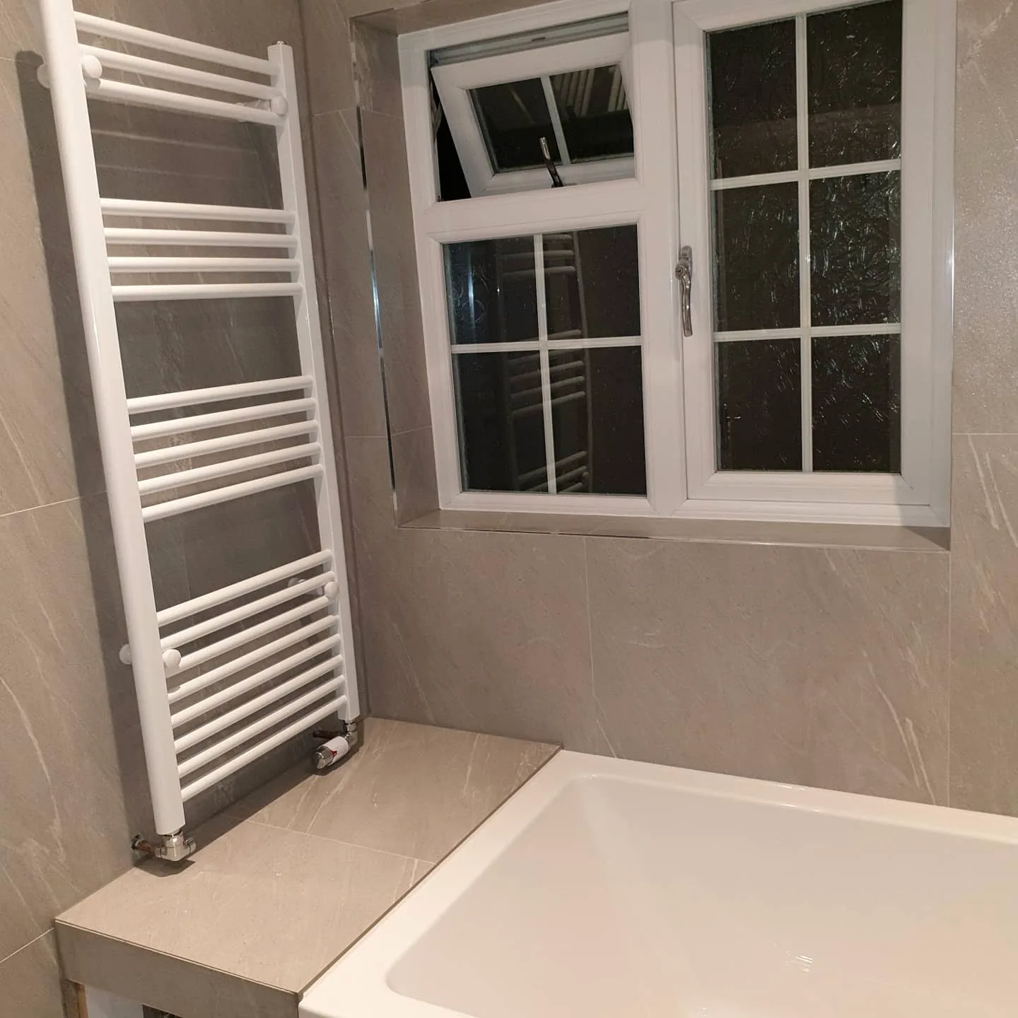 Grey tiled bathroom with bath surround, window and heated towel rail
