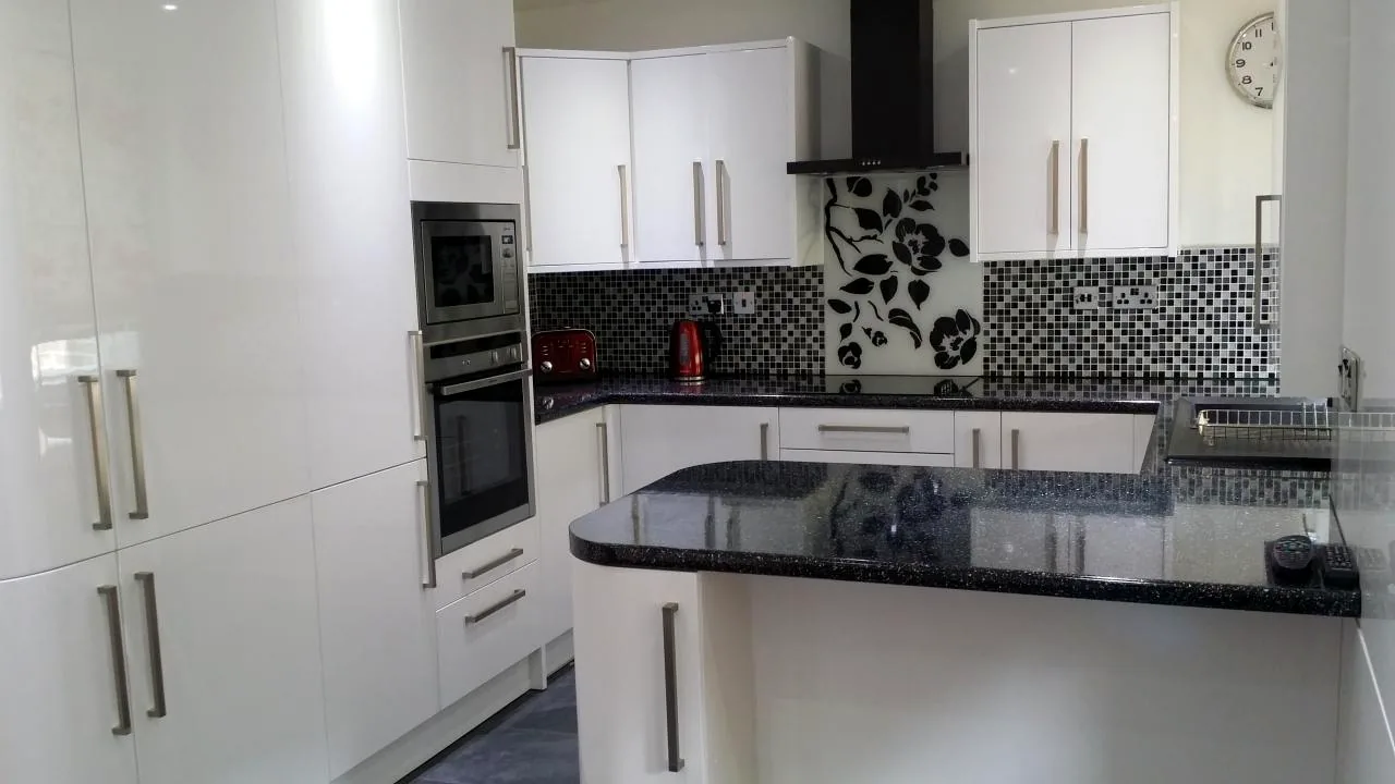 White fitted kitchen with black granite worktops and patterned splashback