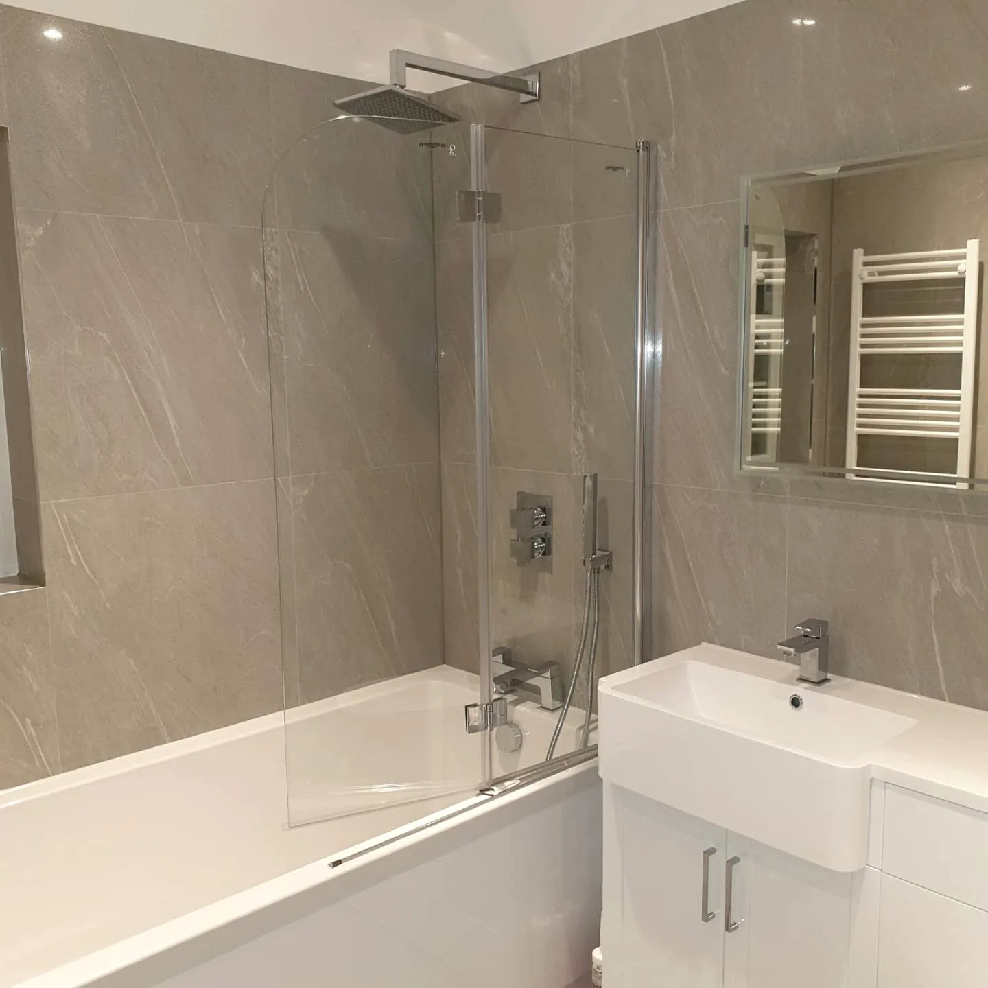 Grey tiled bathroom with bath, rain shower and fitted vanity unit